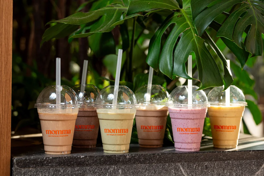 Fileira de smoothies proteicos da Momma sobre mureta com plantas
